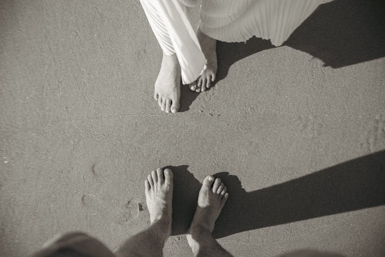 Artistic black and white image of a couple's feet on a sandy beach, capturing a romantic moment.